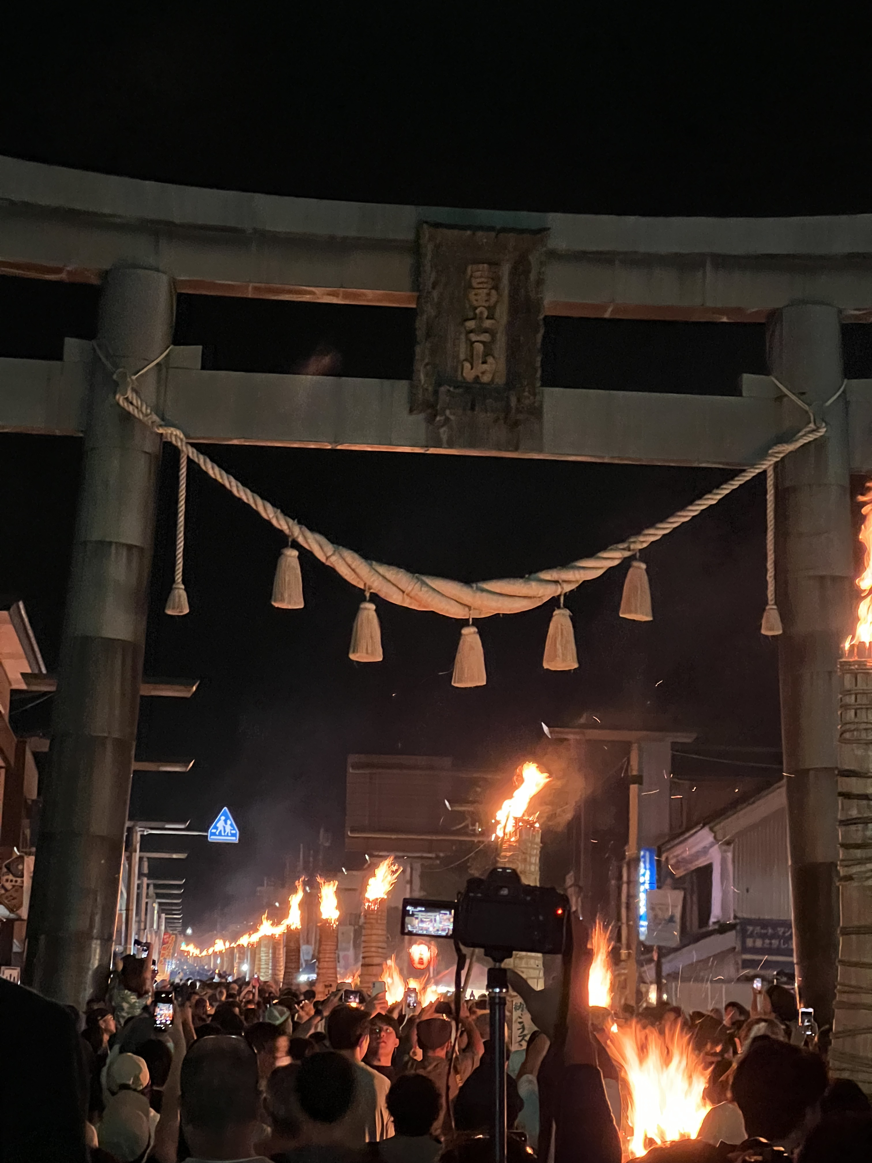 道路を跨る巨大な鳥居の向こうにいくつもの火のついた松明が並んでいる