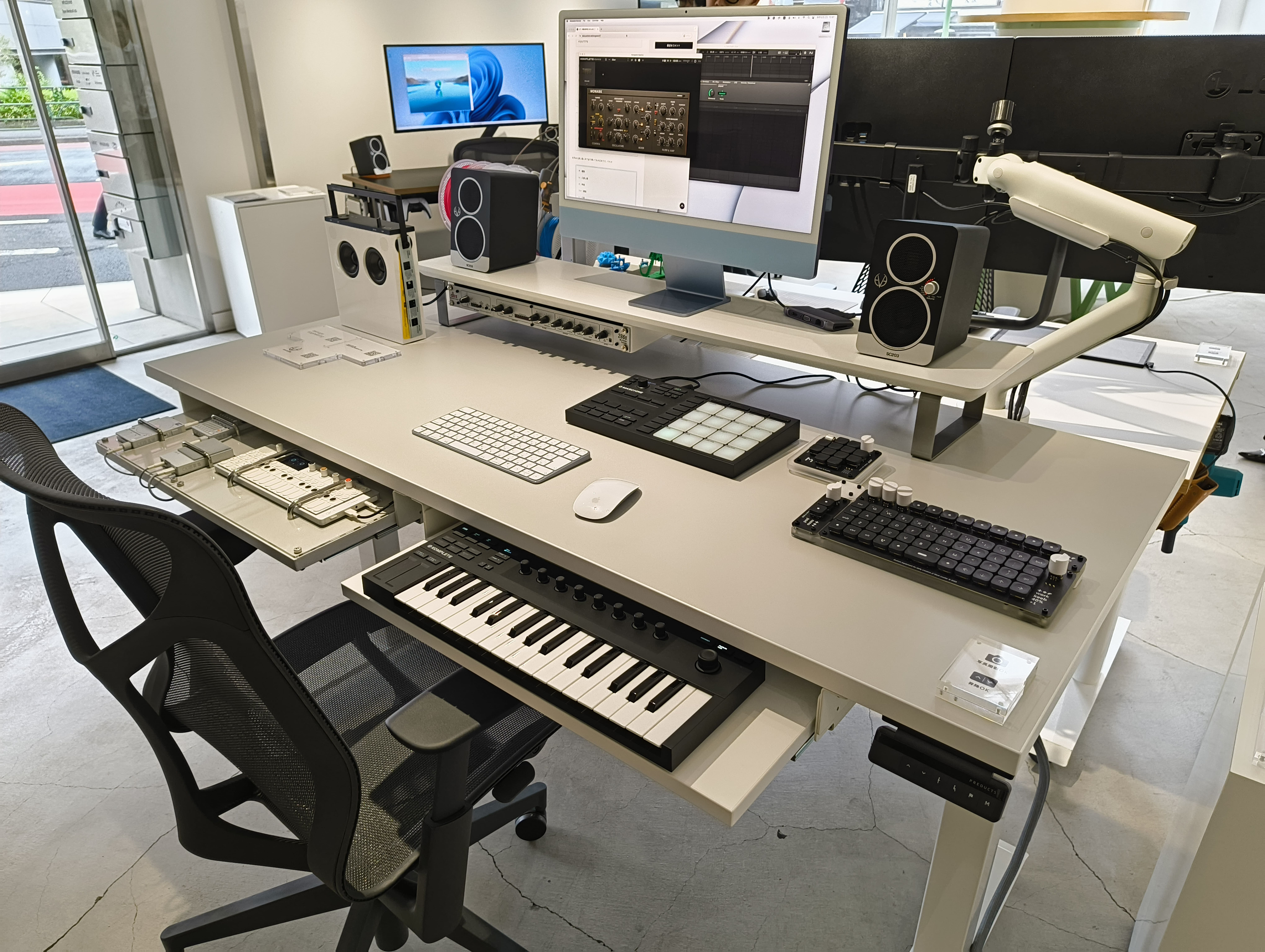 グレーのデスクに teenage engineering のデバイスや楽器のキーボードが並べられている。