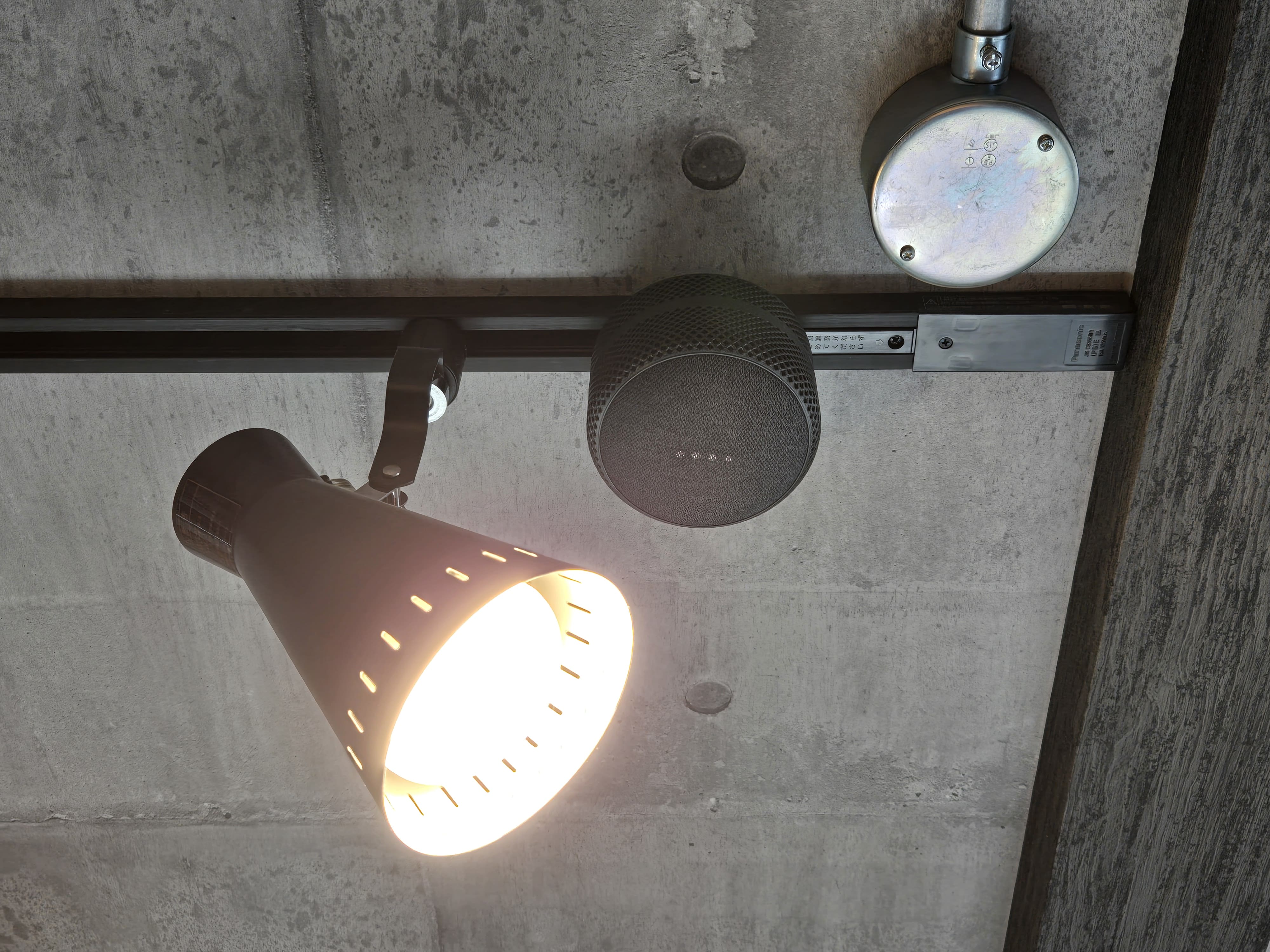黒いダクトレールに黒い Google Nest Mini がついている。隣には黒いスポットライトが並んでいる。