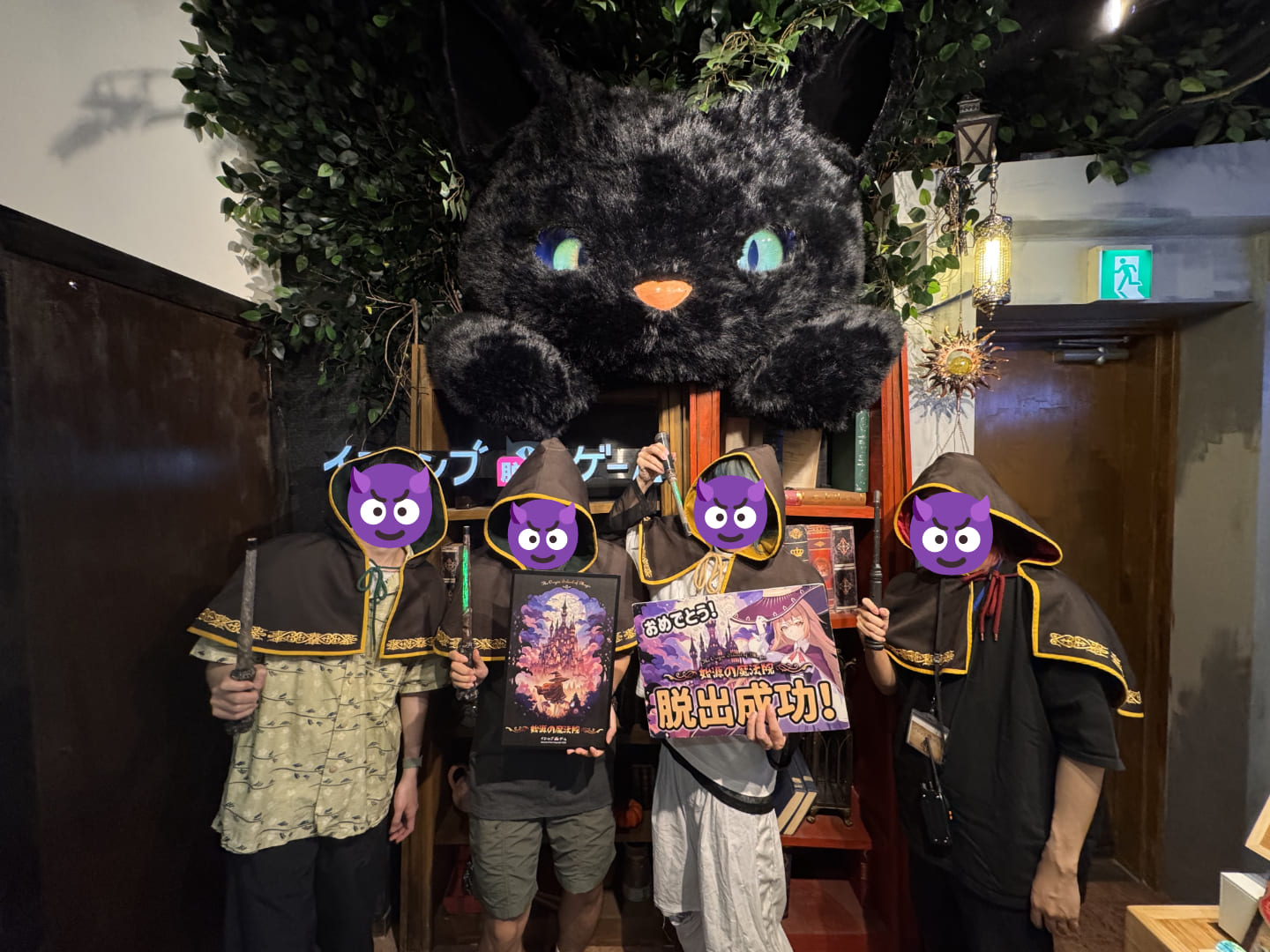 4人の男性が魔法のローブを被って魔法の杖を持って、大きな猫のぬいぐるみの前に並んでポーズを決めている。