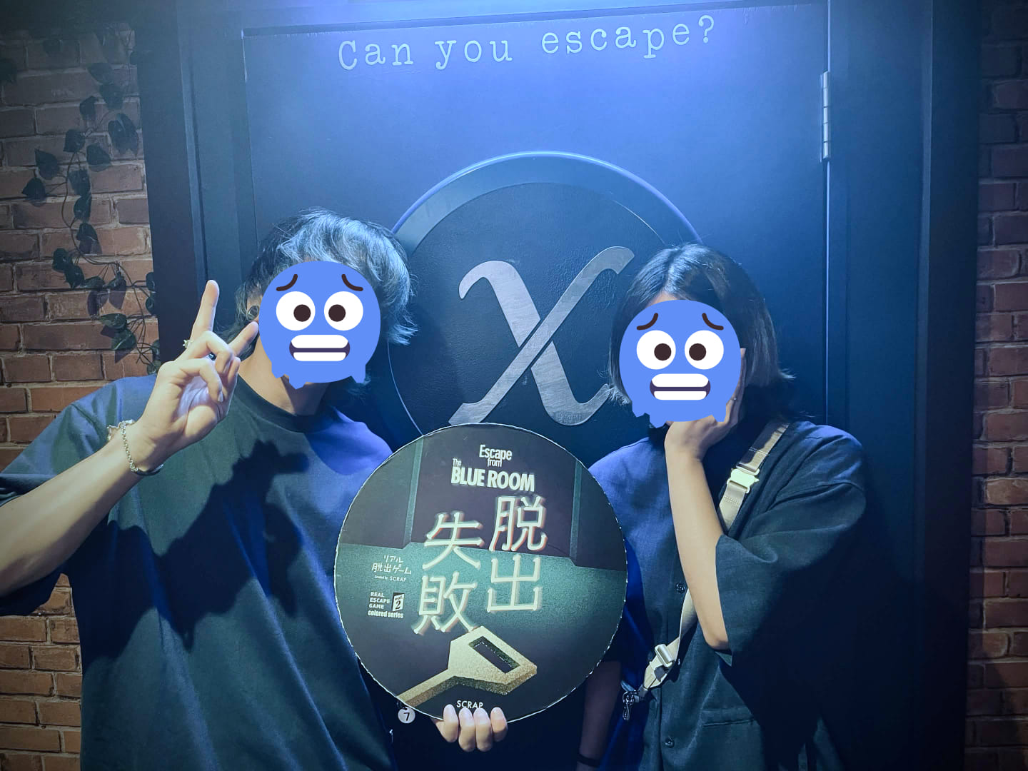 「Can you escape?」と書かれた青い扉の前で2人の男女が並んでいる。「脱出失敗」と書かれたパネルを持っている。