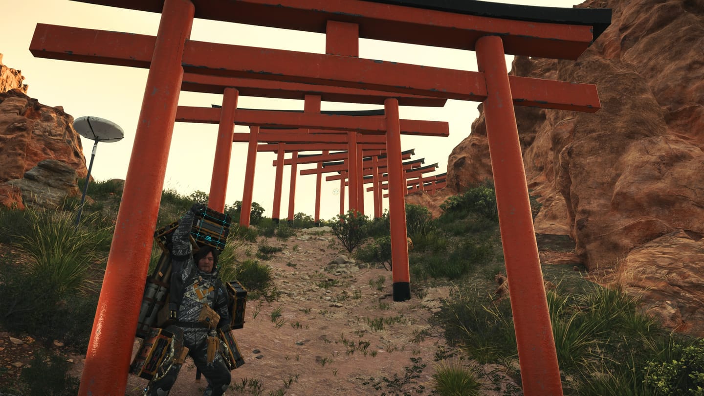 伏見稲荷の千本鳥居的なエリアも見つけられた。 ゲーム『DEATH STRANDING 2: ON THE BEACH』のゲーム画面のキャプチャ。乾燥地帯の荒野のような場所に似合わない日本の鳥居が10本ほど連続で連なって建てられている。先頭の鳥居の下で男性がポーズを取っている。