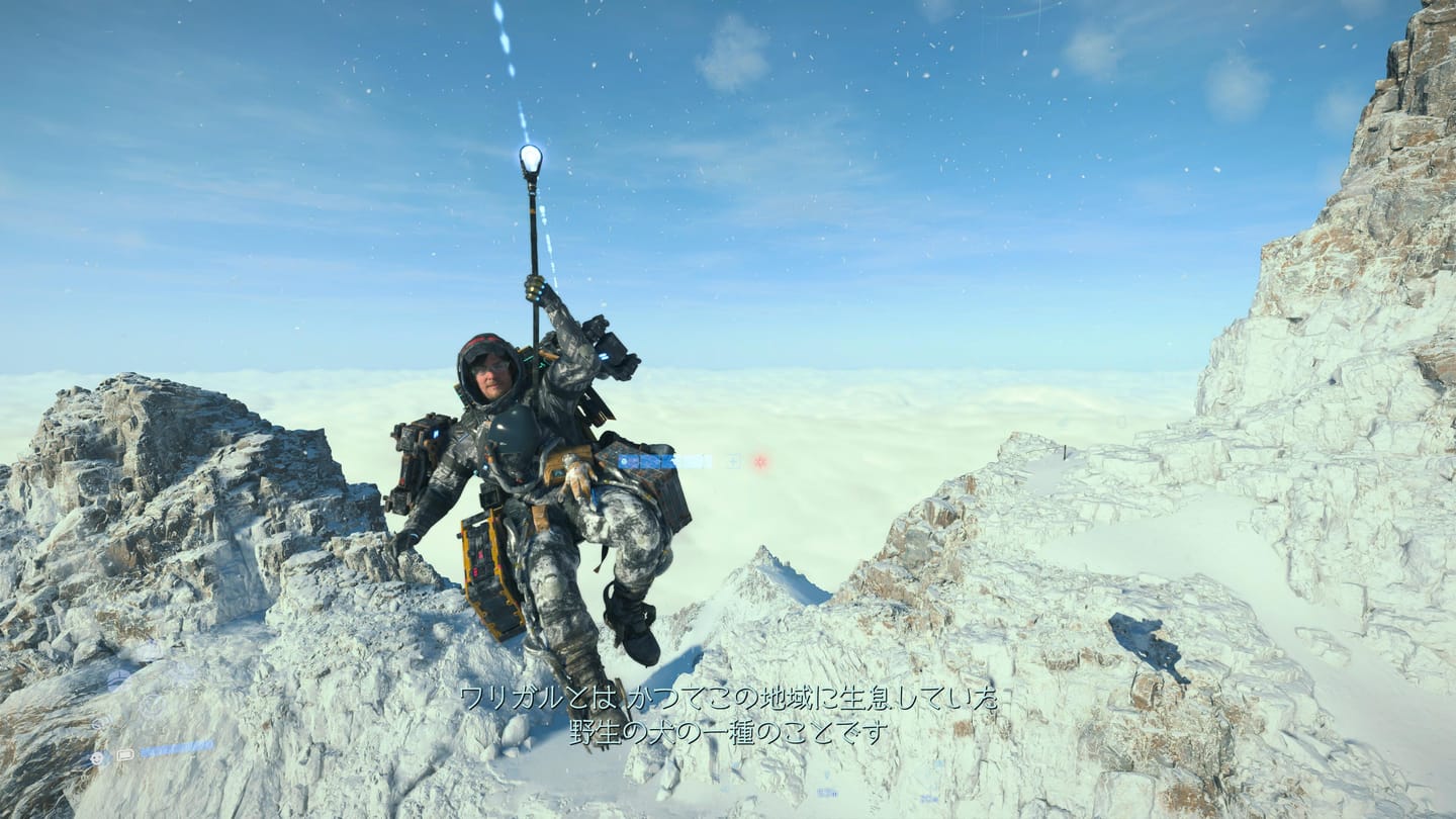 ジップラインを敷いて雪山を一瞬で上り下りする気持ちよさたるや。 ゲーム『DEATH STRANDING 2: ON THE BEACH』のゲーム画面のキャプチャ。雪山頂上付近のゴツゴツした岩場の上に敷かれたロープに吊り下がって男性が滑空している。後ろには雲海が見えていて、その上は空が晴れ渡っている。